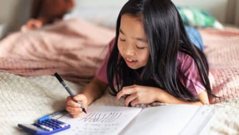 Little girl lying on a bed and doing the homework.