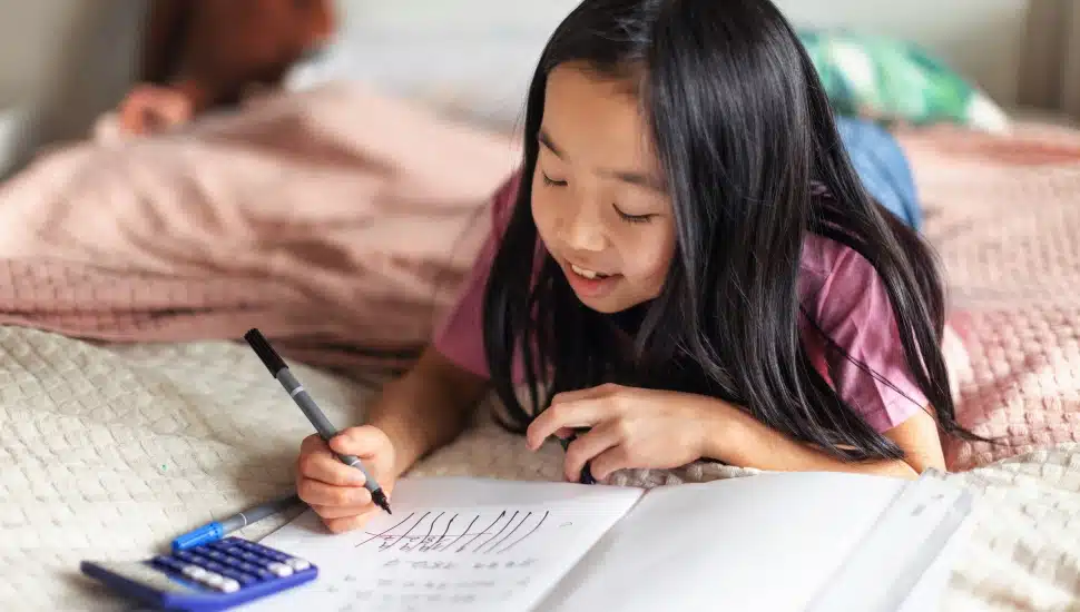 Little girl lying on a bed and doing the homework.