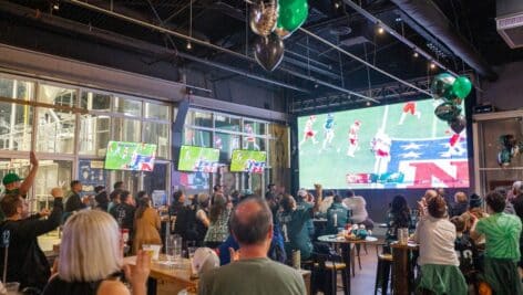 Crowd cheering on eagles on projector screen wearing jerseys inside of Craft Hall warehouse in Philadelphia