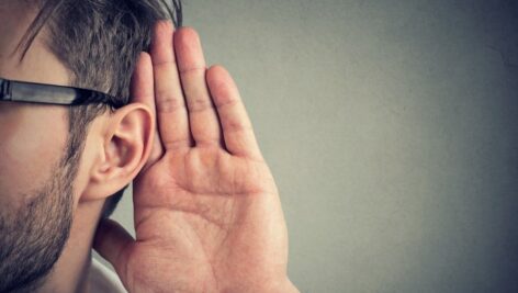 man holds his hand near ear and listens carefully isolated on gray wall background