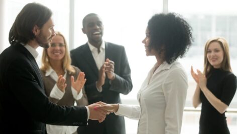 Grateful boss handshaking promoting businesswoman congratulating with career achievement promotion while colleagues applauding