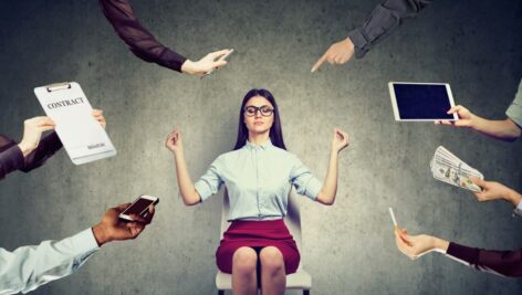 Young business woman is meditating to relieve stress of busy corporate life surrounded by arms holding different objects