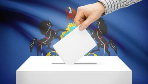 hand dropping ballot into ballot box in front of Pennsylvania state flag