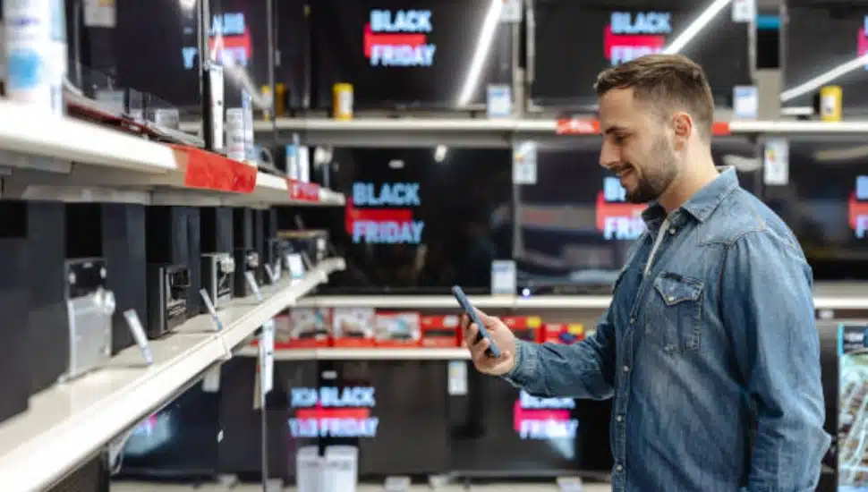A man browsing electronics in a store with Black Friday signs surrounding him.