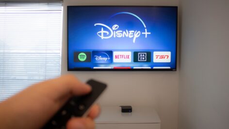 A person holds an Apple TV remote using the new Disney+ app on a Vizio TV