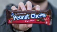 A hand holding a "Goldenberg's Peanut Chews" Original Dark.