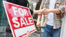 Real estate agent holding for sale sign and shaking hand of customer