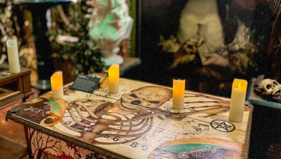 Candles on top of a talking board table with a painting in the background.