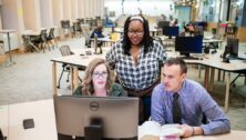 College students gather at a computer to work on their online degree.