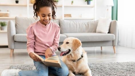 A young girl reads a book with dog by her side