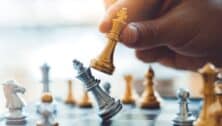 person's hand in corner moving white chess piece and knocking the silver one off its place on the board