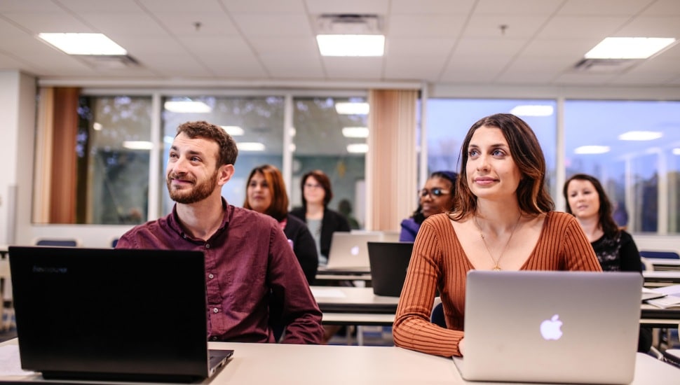 Neumann University students sitting in a classroom in front of laptop computers.