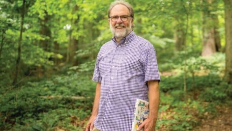 Michael Weilbacher in the forest, holding his new book.