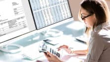 Woman using calculator with paper work and computer in front of her