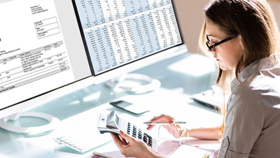 Woman using calculator with paper work and computer in front of her