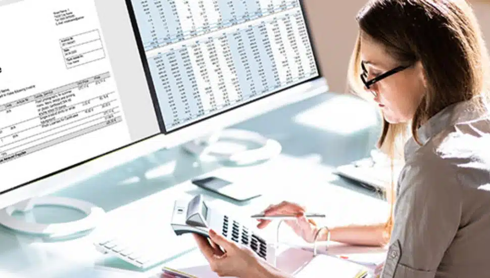 Woman using calculator with paper work and computer in front of her