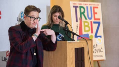 Author Sara Novic speaks at the Free Library of Philadelphia with an interpreter and book cover in the background