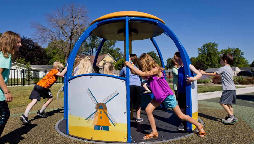 Children playing on a playground spinner. Playground spinners are a great addition to your playground design.