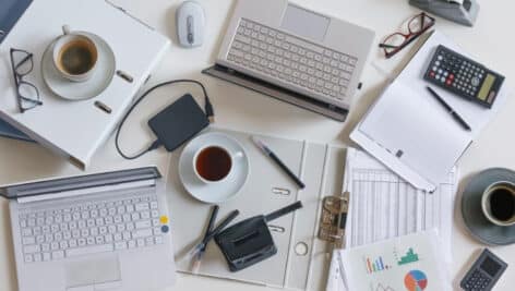 Top view of a full business desk with laptops, accounting papers, calculator, coffee and other office supplies, success work or stress concept, high angle shot