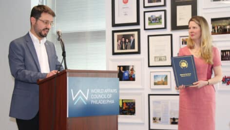 Lauren Swartz holds citation from the City of Philadelphia, while Pierre-Olivier Lugez speaks at the podium.