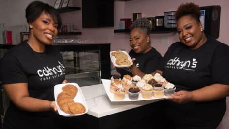 The three lead executives at Cathryn's Cake Salon hold trays of cookies and cupcakes