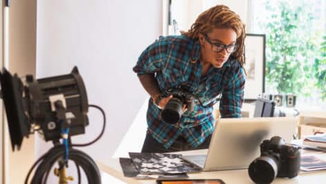 Man with camera in hand using a laptop.