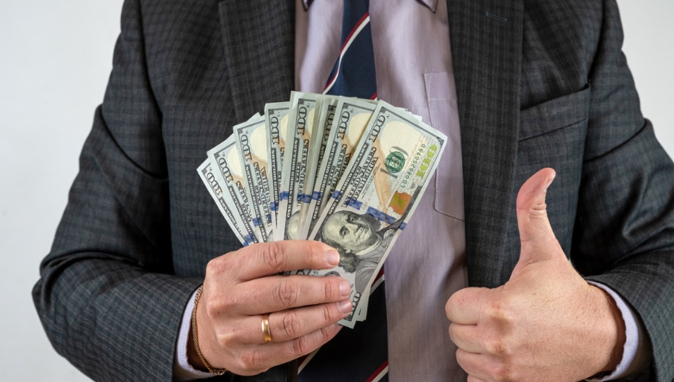 Man holds a stack of money and holds a thumbs up.