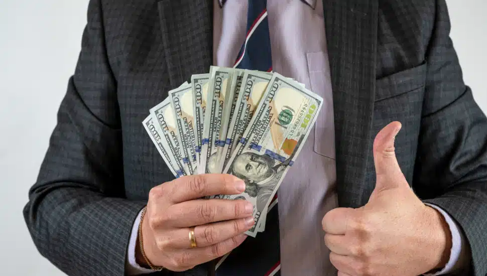 Man holds a stack of money and holds a thumbs up.