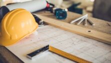 Hardhat sitting on top of construction tool and blueprints.