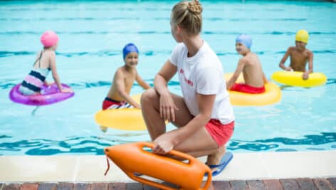 Lifeguard holding rescue can while children swimming in pool.