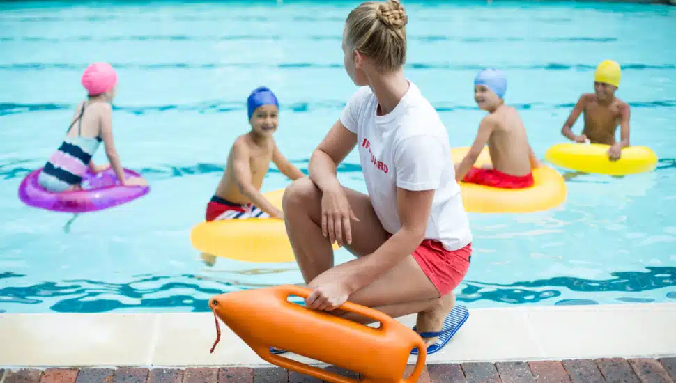 Lifeguard holding rescue can while children swimming in pool.
