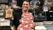 Man smiles with stack of raw meat in front of him.