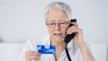 An older woman reading her credit card information to someone on the phone.