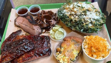 Barbecue ribs, mac and cheese, sauce, greens, and more on a tray.