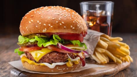 A cheeseburger, glass of cola and french fries on wooden tray.