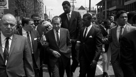 Wilt Chamberlain walking behind Richard Nixon and a group of supporters and reporters.