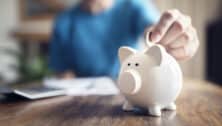 Man putting a coin into a pink piggy bank concept for savings and finance.