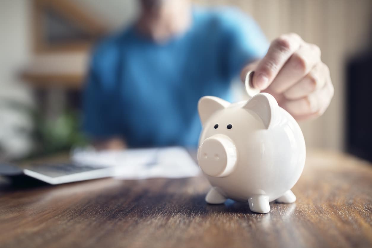 Man putting a coin into a pink piggy bank concept for savings and finance.