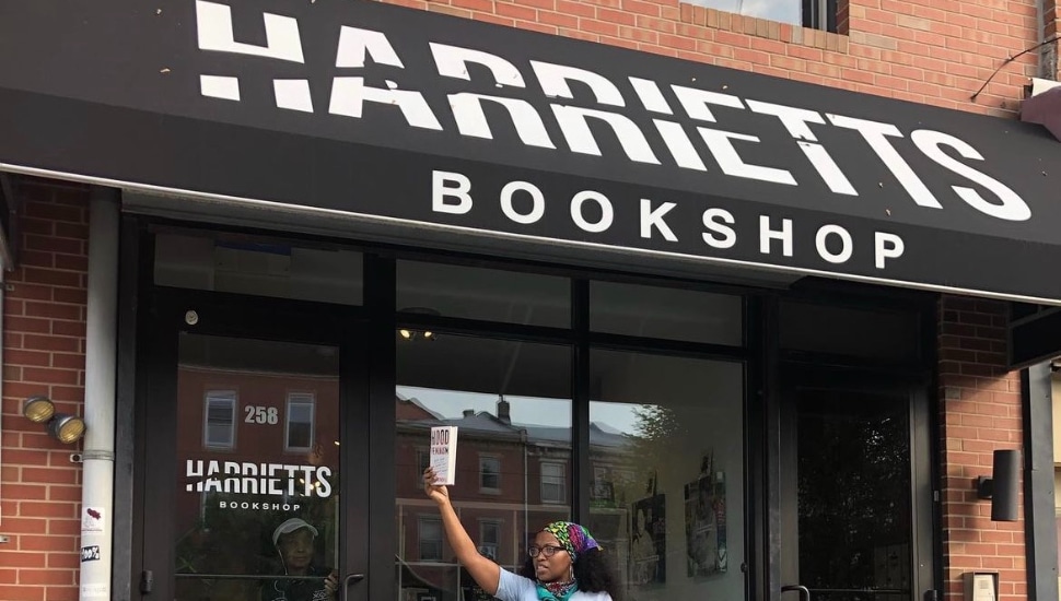 Harriett's Bookshop storefront with owner Jeannine A. Cook pointing to the sign.