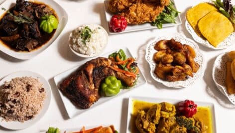 A table with various Jamaican dishes, include rice and beans, chicken, patties, and more.