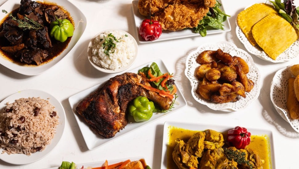 A table with various Jamaican dishes, include rice and beans, chicken, patties, and more.