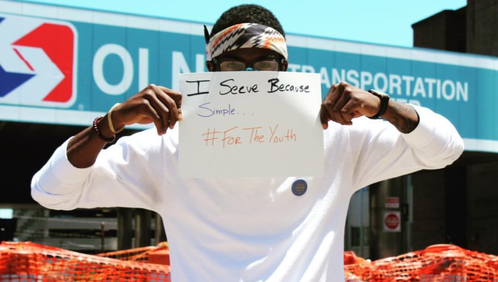 Young man holds sign that says, "I Serve Because Simple ... #ForTheYouth