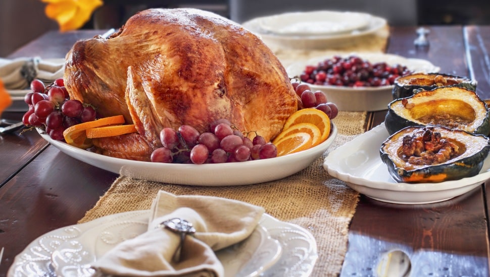 Delicious golden roasted Thanksgiving turkey on a platter garnished with fresh grapes and slices of oranges on a rustic farmhouse table.