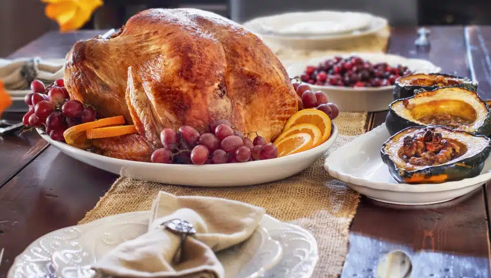 Delicious golden roasted Thanksgiving turkey on a platter garnished with fresh grapes and slices of oranges on a rustic farmhouse table.