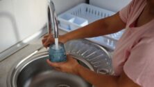 A person fills a glass with clean water from a kitchen faucet.