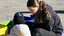 Amelia Fletcher sits on a foam mat playing with a small child.