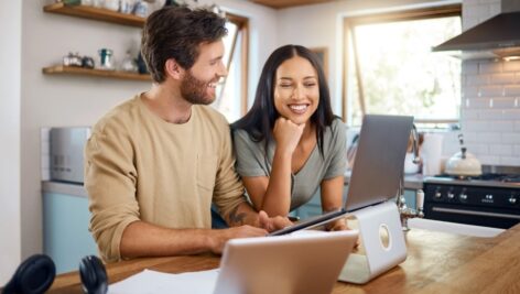 Young couple works on a laptop computer in the kitchen.