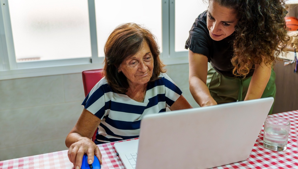 Middle-aged daughter teaching elderly mother to use a laptop, being a digital navigator.