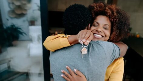 Minority couple hugs after achieving dream of homeownership.