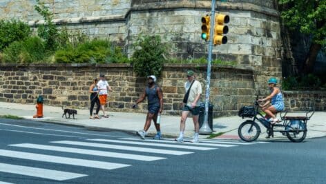 A group of people crossing the street, walking, and biking.